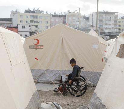 personne en situation de handicap en fauteuil roulant entre des tentes de campement