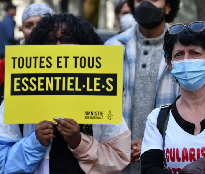 Une personne en ;anifestation tient une pancarte "Toutes et tous essentiel·le·s"