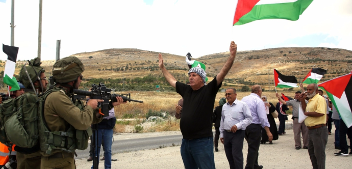 Des palestiniens avec drapeaux devant des militaires armés