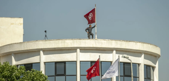 Un militaire tient un drapeau tunisien sur le toit d'un bâtiment 