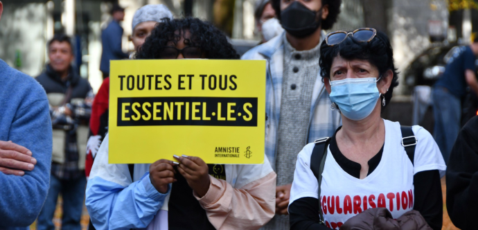 Une personne en ;anifestation tient une pancarte "Toutes et tous essentiel·le·s"