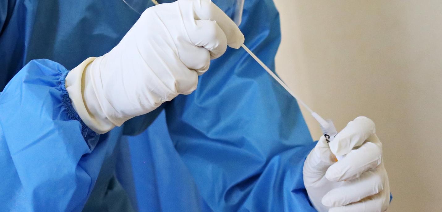Une personne vêtue d'une blouse médicale bleue et de gants tient un échantillon dans ses mains.