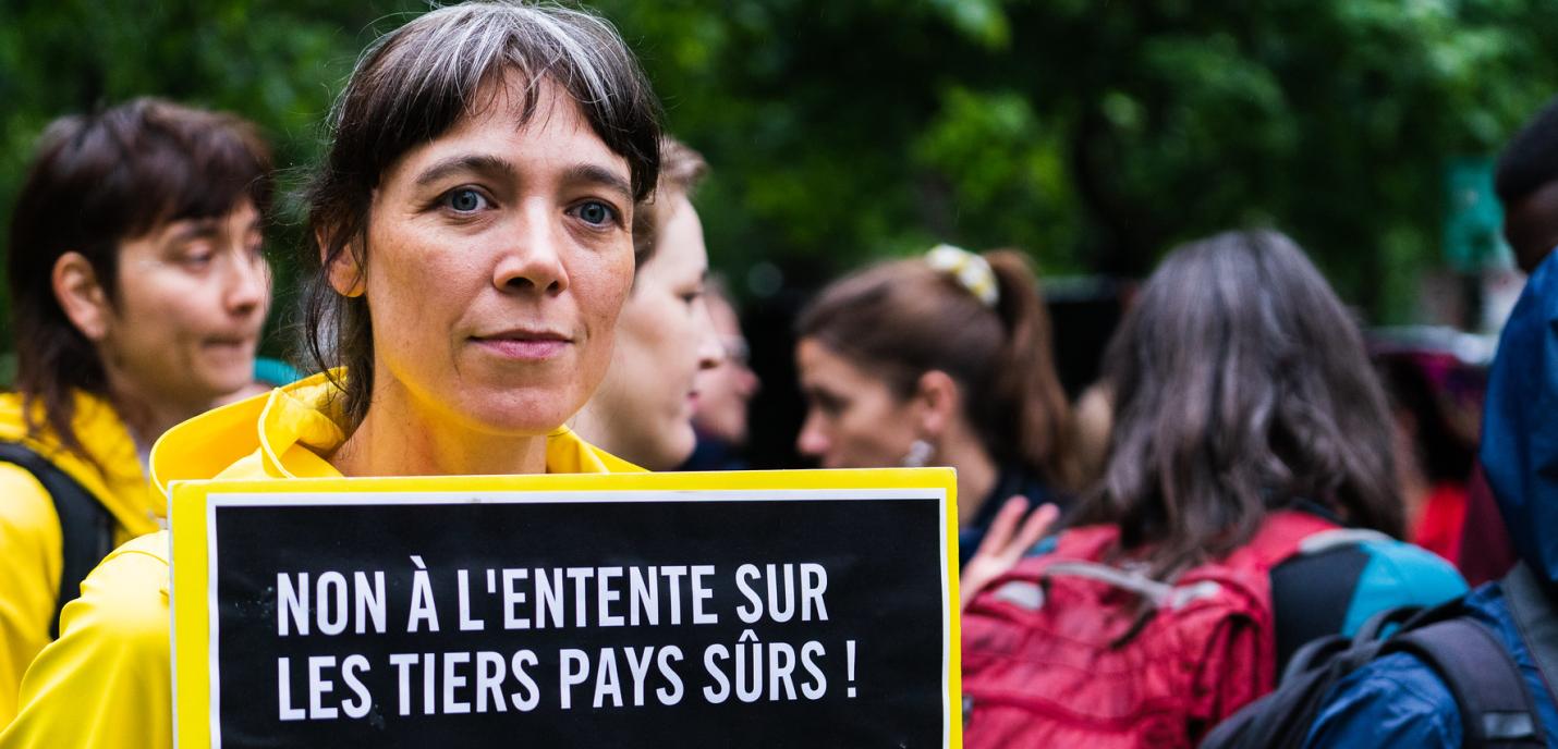 Personne tenant une pancarte "Non à l'entente sur les tiers pays sûrs ! Oui à l'accueil des réfugié·e·s !"