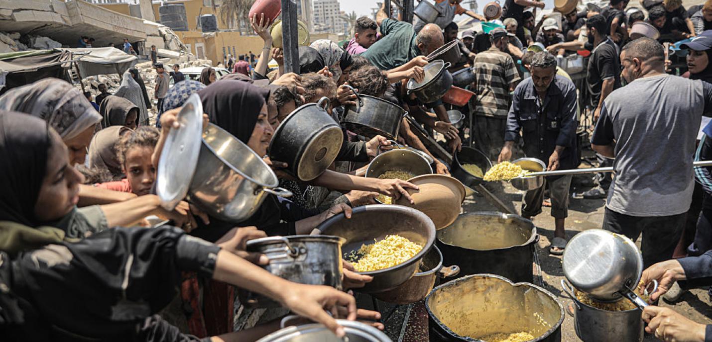 Un groupe de plusieurs personnes qui sont tassés l'un contre l'autre de manière très détresse qui essaient désespérément de remplir leur contenaires de nourritures sachant qu'il yen a trés peu et que c'est une famine