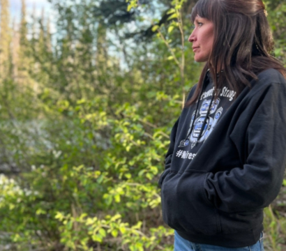 Une femme portant un sweat à capuche noir et un jean bleu regarde vers une rivière.