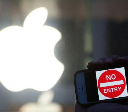Un téléphone tenu dans une main affiche le message "No Entry" sur son écran, tandis qu'en arrière-plan, le logo lumineux d'un magasin Apple.