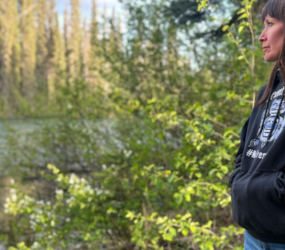 Une femme portant un sweat à capuche noir et un jean bleu regarde vers une rivière.