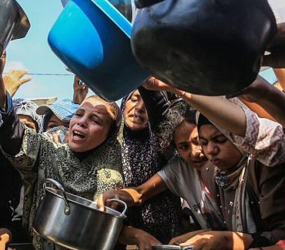 Groupe de femmes et d’enfants brandissant des casseroles et des récipients vides dans une foule, exprimant la faim et le manque de nourriture, scène de crise humanitaire.